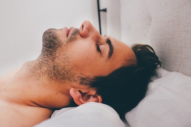 Muž so zatvorenými očami leží v posteli 